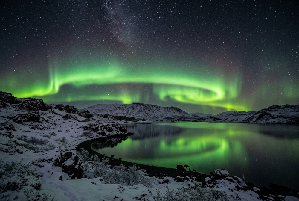 Northern Lights glowing green over snow-dusted mountains in Iceland