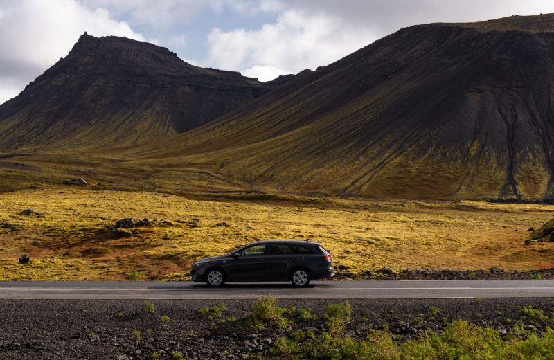 Kia Ceed Station Wagon driving on a paved road below mossy mountains in Iceland